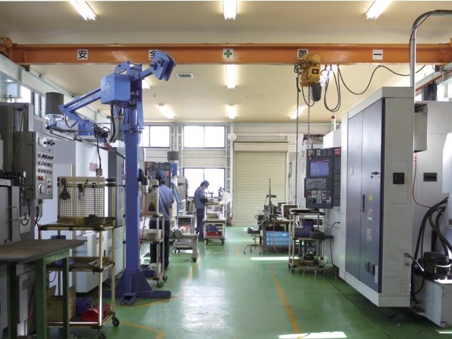 天井クレーンと工作機械が並ぶ加工工場。奥で従業員が作業している