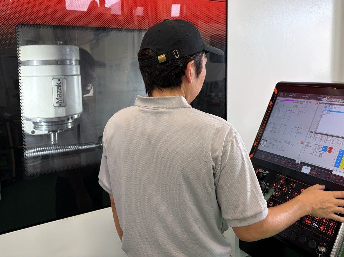 マシニングセンタの操作盤を操作する従業員。左奥に加工中の主軸が見える